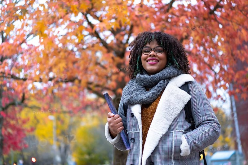 Portrait of black ethnic girl strolling in university college under fall foliage trees on back to school