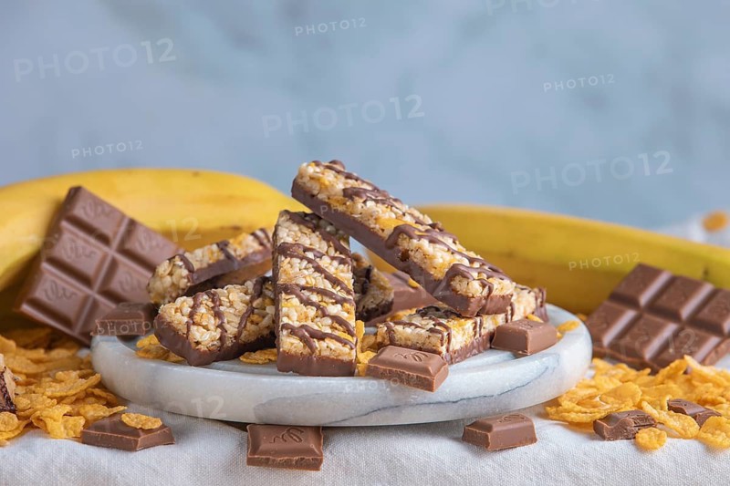 Muesli bar on a plate surrounded by chocolate, bananas and cornflakes