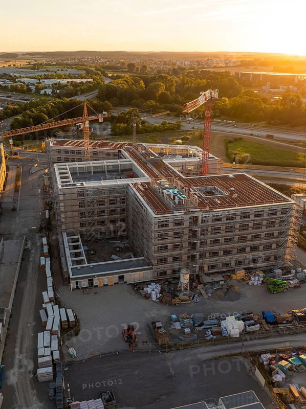 Constructed building and construction site with cranes in an urban environment at sunset, new hospital building, Böblingen airfield, Germany