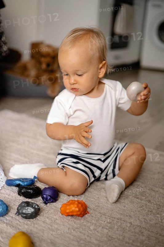 Baby in striped shorts playing with colorful toys on a rug