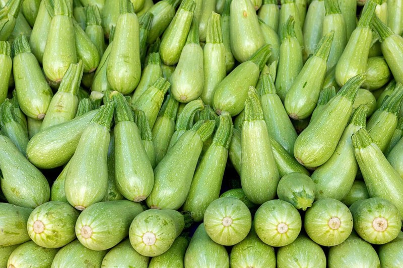 A neatly stacked pyramid of light green squash displayed at a market