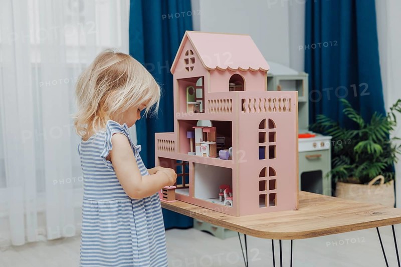 Blonde Toddler Girl playing with pink doll house in children room