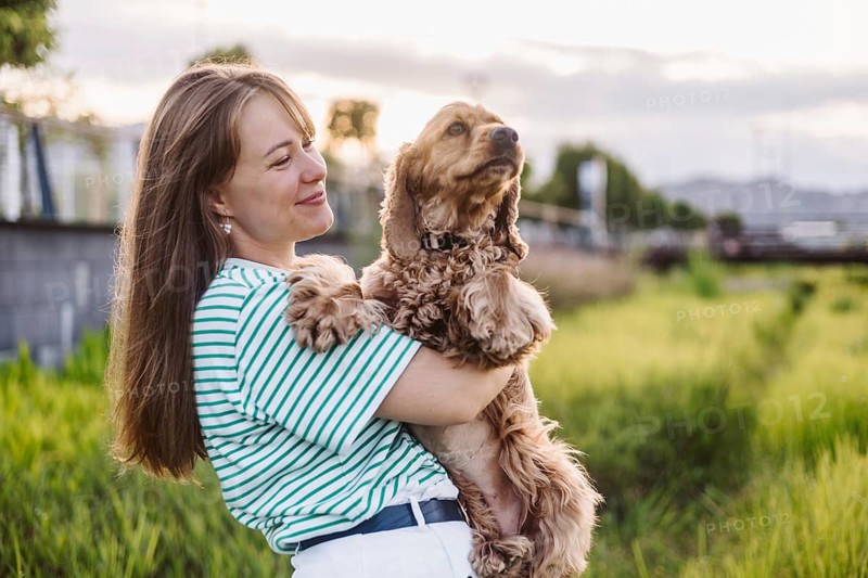 A woman affectionately holding her dog Cocker Spaniel in a park during the evening
