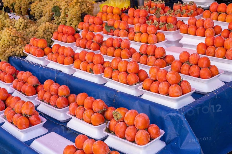 Orange persimmons neatly arranged on white trays at a market display