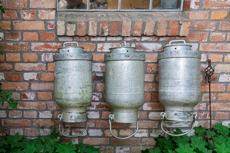 Three old milk cans hang in front of a brick wall that gives off a rustic atmosphere, North Rhine-Westphalia, Germany