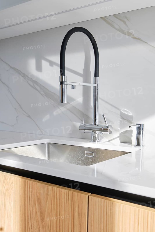 A contemporary kitchen showcases a stylish faucet with a flexible neck installed over a polished marble countertop. The wood cabinetry adds warmth, creating a sophisticated atmosphere