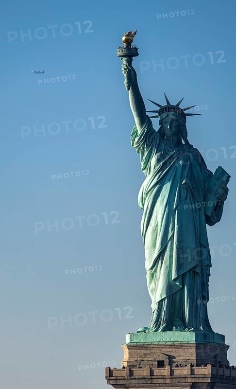 Majestic view of the Statue of Liberty standing tall in New York against a serene blue sky backdrop, featuring a distant airplane