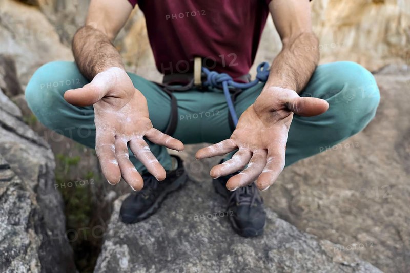Close-up of a climber's hands showing the strength needed for rock climbing. The image highlights the texture and markings on the climber's gri