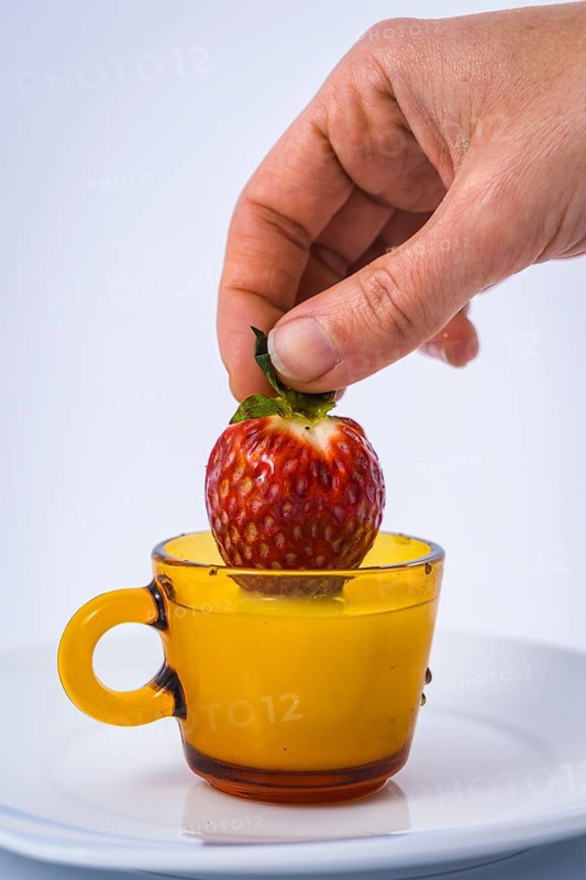 A strawberry inside a milk cup by a woman hand with white background