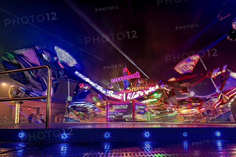 An illuminated carousel in full motion at night, surrounded by colorful lights at a fair, carousel and the hustle and bustle of summer winnings in Eisenach