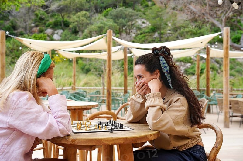Family enjoy a lively game of chess at a cozy outdoor cafe Surrounded by lush greenery, they share laughter and strategic moves under shaded canopies