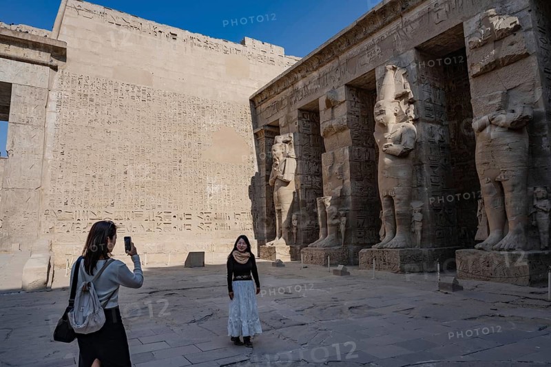 Foreign tourists admire the reliefs and hieroglyphs inside Medinat Habu, the ancient Egyptian Mortuary Temple of Ramesses III on the West Bank of The Nile, Luxor, Egypt
