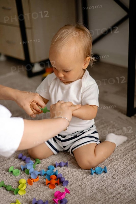 A toddler is aided by an adult while playing with colorful toys, capturing a moment of guidance