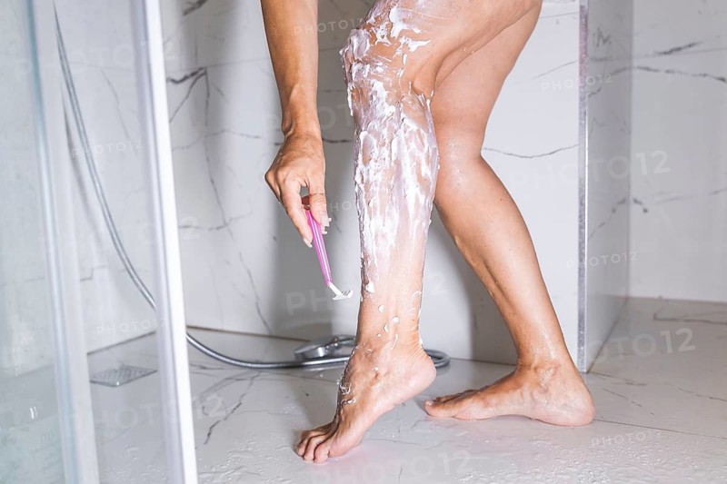 Mature woman, legs and hair removal in bathroom with shaving for skincare, body wellness and morning routine in home. Person, razor and cream for grooming, hygiene and pamper for self care