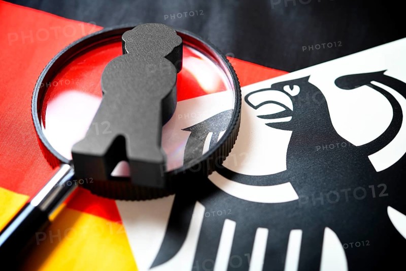 Magnifying glass with spy figure on federal eagle and German flag, symbolic photo of German secret service reform +++ editorial use only