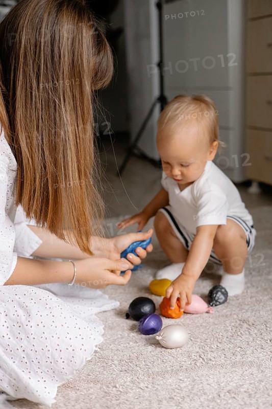 A mother interacts with a toddler playing with colorful toys on the floor, highlighting learning and connection