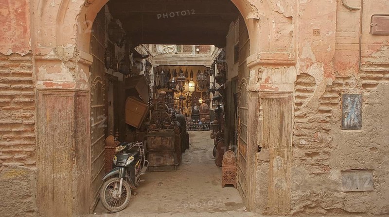 An arch in the old town leads to a Moroccan courtyard in the medina full of antique furniture, with a motorcycle in front, Marrakech, Morocco