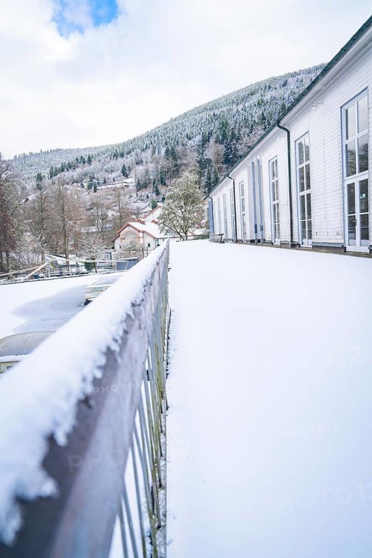 Snow-covered terrace with a view of mountains and a building under a blue winter sky, spa garden, Bad Wildbad, Black Forest, Germany