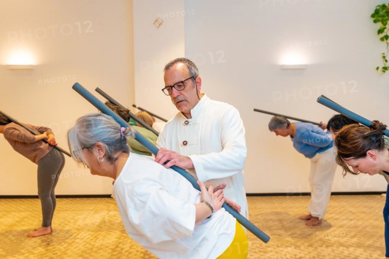 Qi gong class members using tube to stretch the back with the guidance of a male instructor