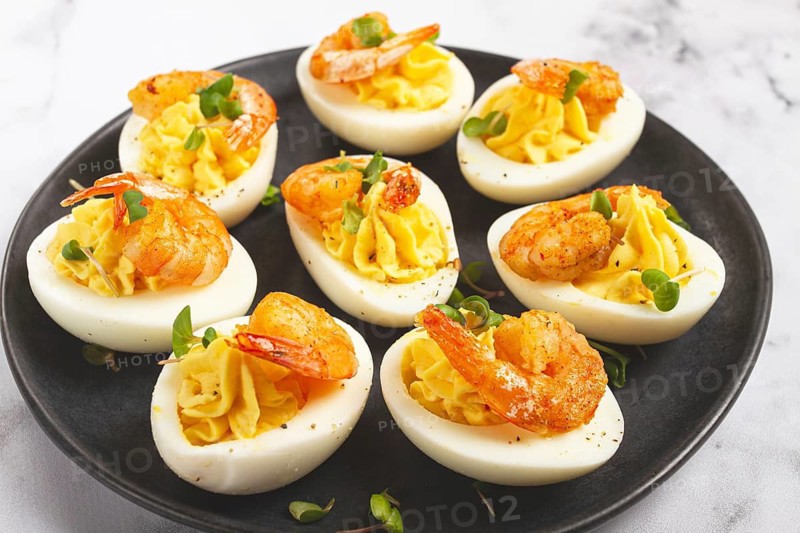 Boiled eggs stuffed with yolk and seasoned with mayonnaise, stuffed eggs with shrimp, on a black plate, selective focus, close-up, no people