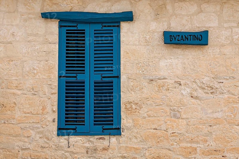 Blue window with wooden shutters on a stone wall next to a sign, Omodos, Cyprus