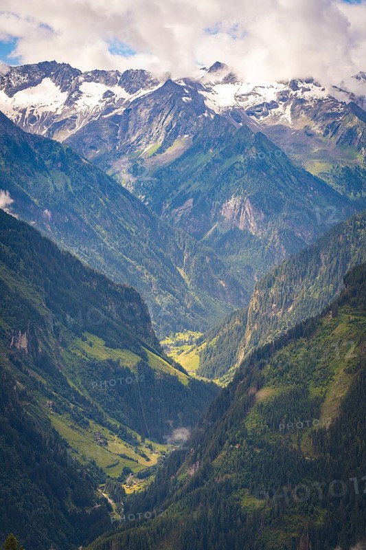 A wide valley stretches between high, partly snow-covered mountains under a blue sky, Stilluptal, Zillertal. Austria