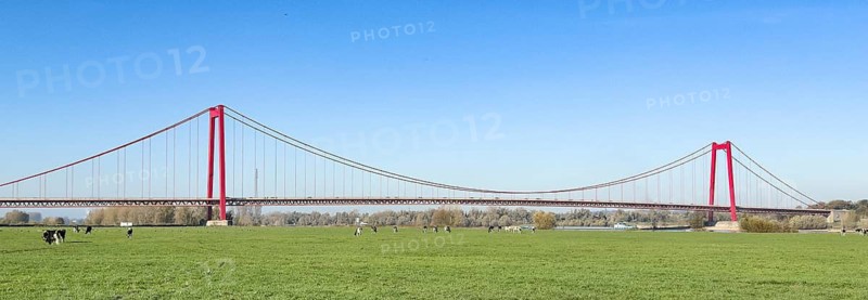 Panorama view over Rhine meadows on the left bank of the Rhine to earth-anchored suspension bridge with two abutments and red steel piers nicknamed Golden Gate of the Lower Rhine over the Rhine river, with a total length of 1228 metres the longest suspension bridge in Germany, Emmerich, North Rhine-Westphalia, Germany