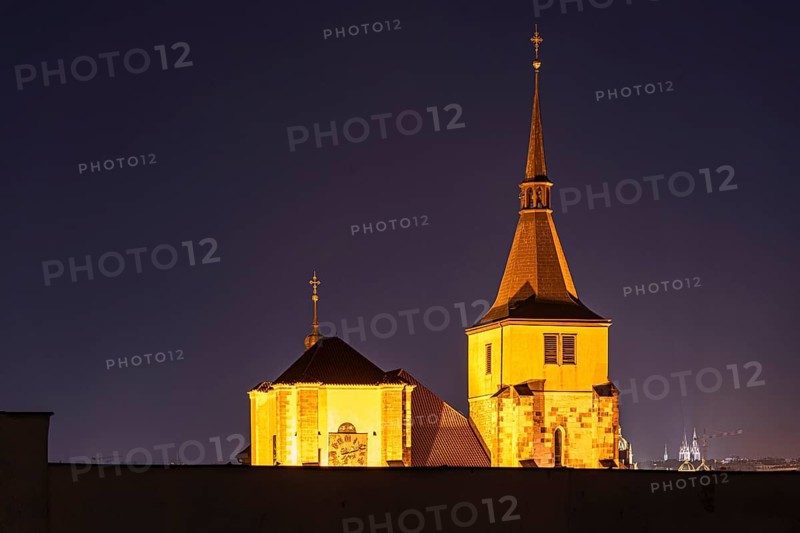A beautiful nighttime view of historic Prague architecture, showcasing illuminated towers and spires against a dark blue sky, highlighting their timeless beauty