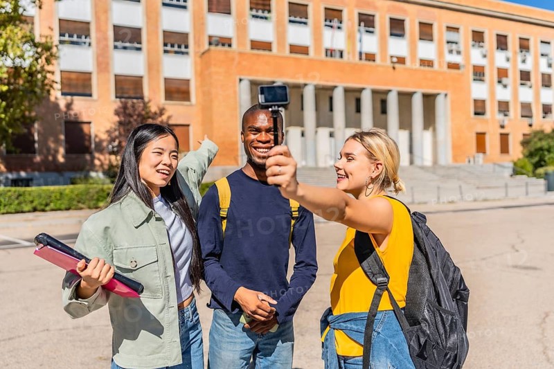 University student recording vlog with friends using a digital portable camera at campus