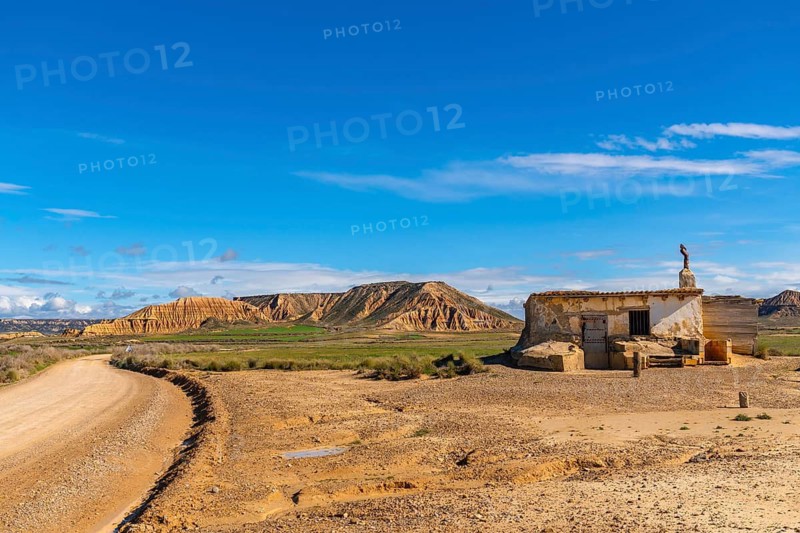 Bardenas reales semi desert natural region in navarre, spain, featuring an old abandoned farmhouse and a dirt road under blue sky