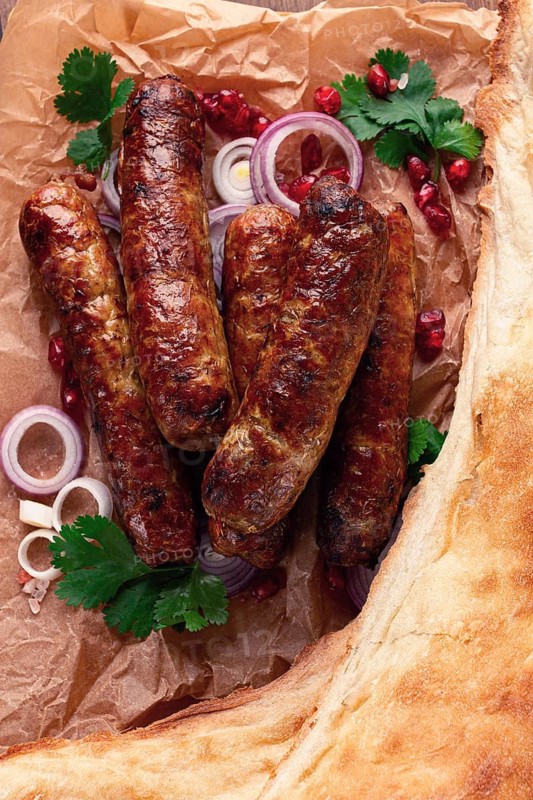 Fried kupaty on parchment, with red onion and pomegranate, kupaty, Georgian cuisine