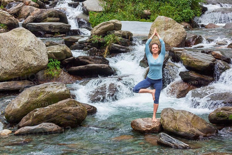 Woman in Hatha yoga balance yoga asana Vrikshasana tree pose at waterfall outdoors