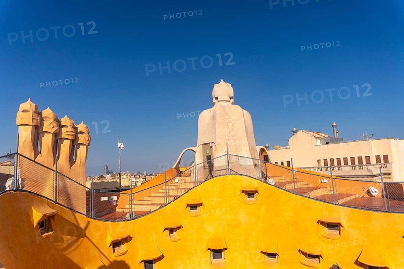 Bright yellow rooftop with unusual chimneys and staircase access under a clear blue sky in barcelona, spain