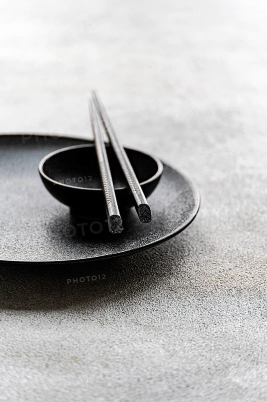 A minimalist table setting in black and white featuring a plate, bowl, and chopsticks. The composition highlights simplicity and elegance, suitable for modern dining aesthetics