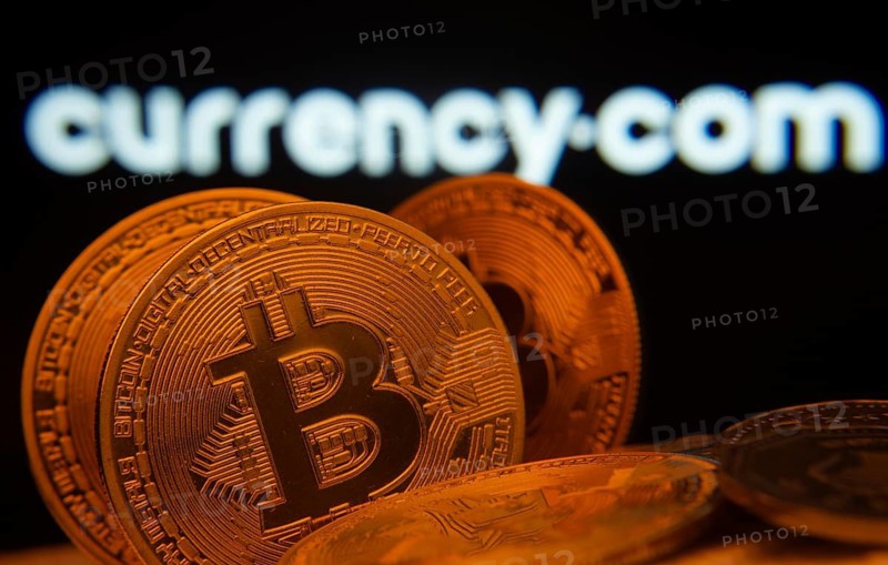 Dhaka, Bangladesh- 22 June 2025: Close-up of Bitcoin coins with the Currency.com logo visible on a screen in the background
