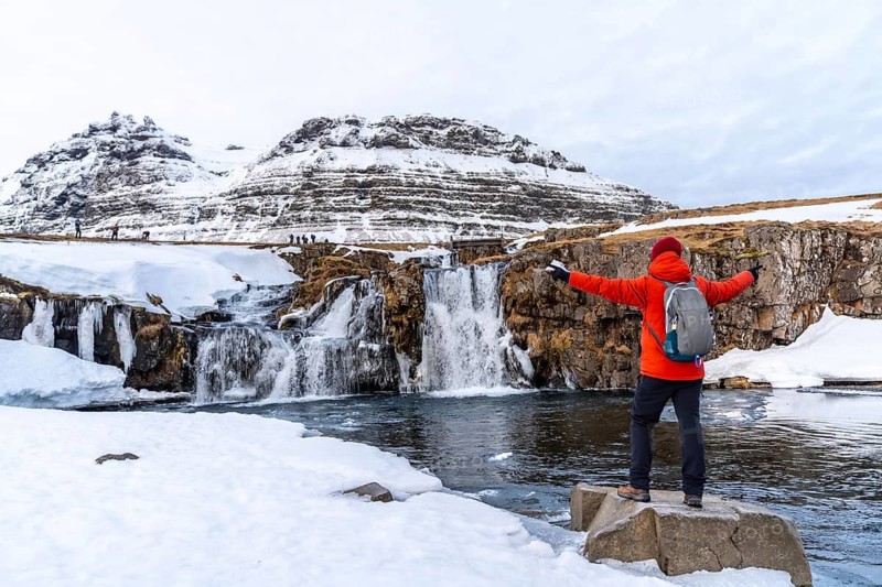 A man with his back turned at the Kirkjufell waterfall in winter in Iceland