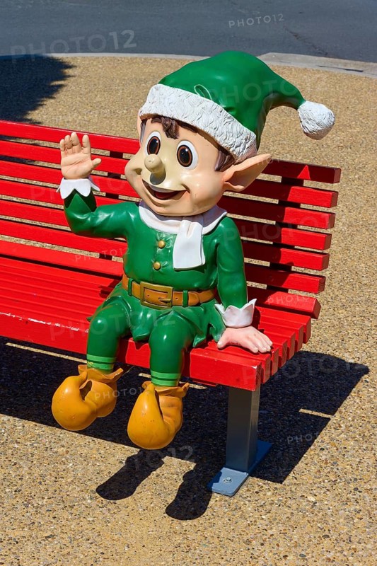 Elf figure in green costume greeting on a red bench in sunny weather, Bethlehem, Tauranga, Bay of Plenty, North Island, New Zealand