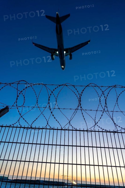Symbolic image security at the airport, outer fence at Düsseldorf International Airport, steel wire fence, with S-wire rolls, NATO wire, on the top of the fence, aeroplane approaching, sunset, North Rhine-Westphalia, Germany