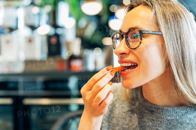 Stylish woman wearing glasses eating a crunchy snack in a cozy cafe
