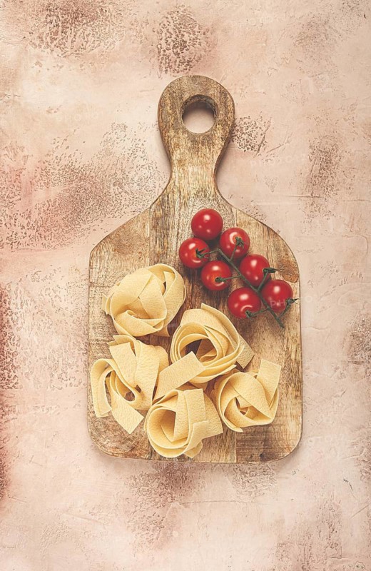Raw pappardelle pasta, on a wooden chopping board, with cherry tomatoes, top view, no people