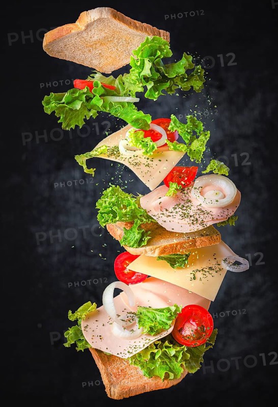 Sandwich with floating ingredients, tomatoes, lettuce, sausage, cheese, onion against a dark background