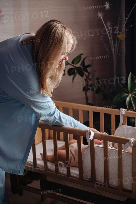 A mother leans over a crib to care for her baby boy in a cozy nursery. The intimate setting is filled with soft light, creating a warm, nurturing atmosphere