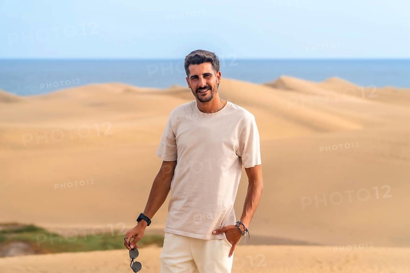 Young man enjoying a summer vacation amidst the stunning desert landscape of maspalomas dunes, basking in the warm sun and vibrant scenery