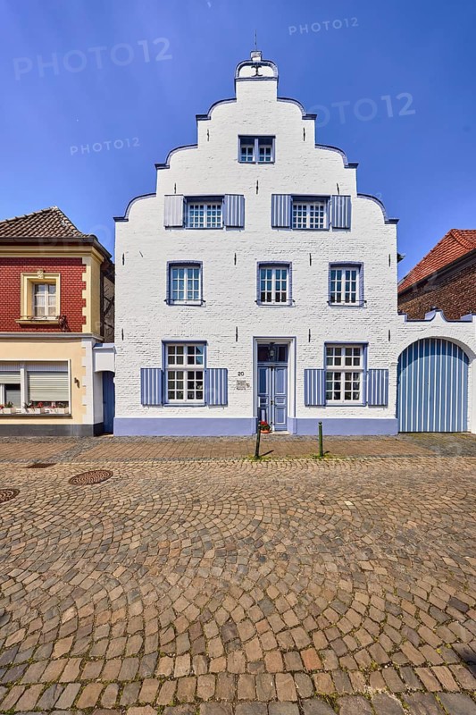 Old town, historic town center, historic town house, houses, façade with windows and shutters, tail gable, gate, door, entrance door, barrier bollard, roadway, street, paving stones, blue sky, cumulus cloud, wine route, Wachtendonk, Kleve district, North Rhine-Westphalia, Germany