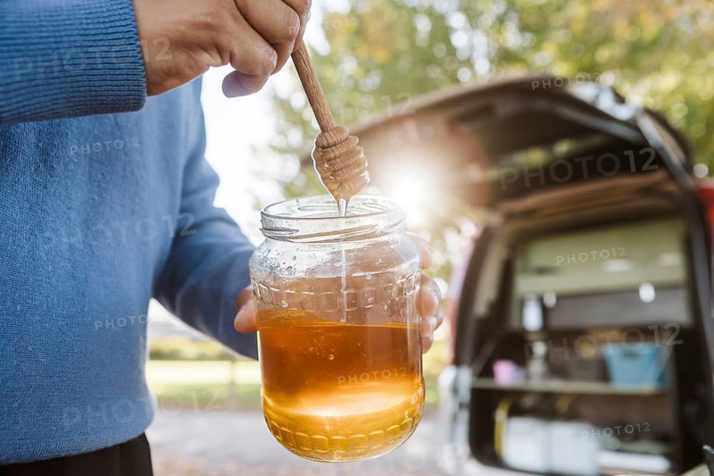 A woman enjoys a delightful breakfast with honey outside her van amidst the vibrant autumn landscape of New Zealand. She embraces nature and tranquility in her outdoor dining experience