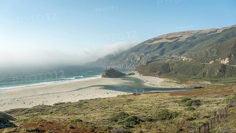 Stunning view of the rugged Big Sur coastline, with rolling hills and the Pacific Ocean shrouded in fog. A perfect combination of natural beauty and serenity