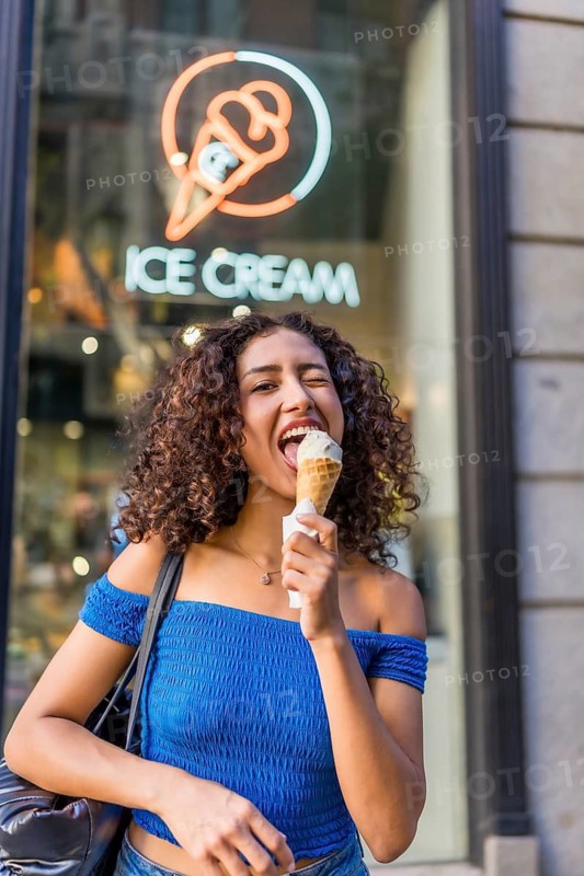Vertical photo of a friendly funny woman grimacing and winking to the camera while eating ice cream outdoors