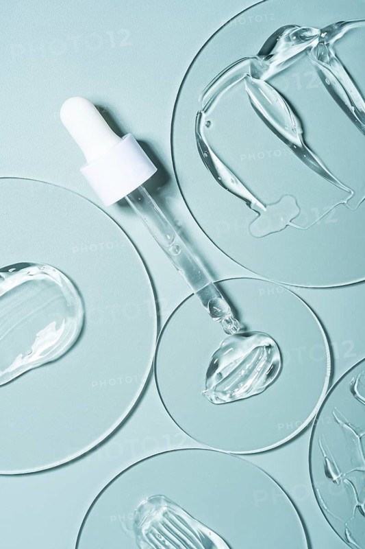 Top view of transparent gel smears and pipettes on laboratory glass plates. The smooth blue background enhances the clarity and texture, perfect for skincare product displays