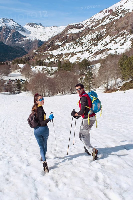 A couple hikes through a snow covered mountain landscape, enjoying the breathtaking winter scenery. They are equipped with backpacks and hiking poles, embracing the adventure