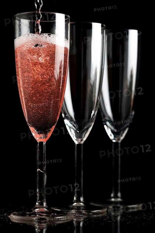 Three champagne glasses in front of a black background, first glass is filled with champagne